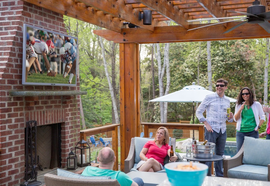 A group of people enjoys a football game on their outdoor TV.