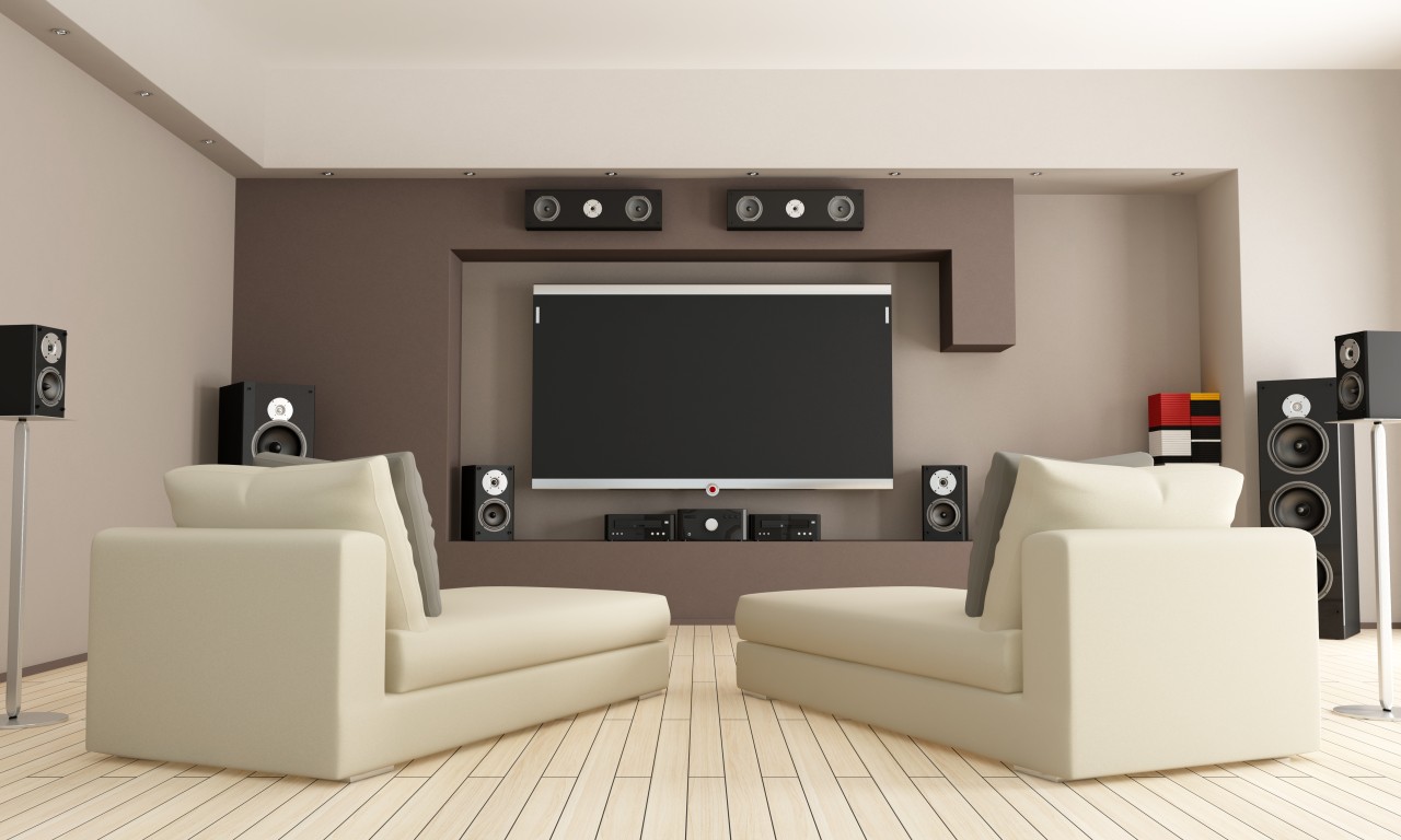 Two living room chairs facing a large flat screen television surrounded with speakers.