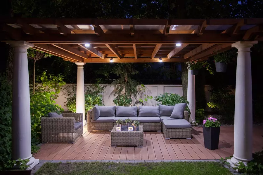 Photo of a cozy, well-lit outdoor space with a couch, chair, coffee table, and accentuated columns. 