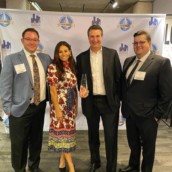 Four people standing together at an award ceremony, one holding an award, all smiling.