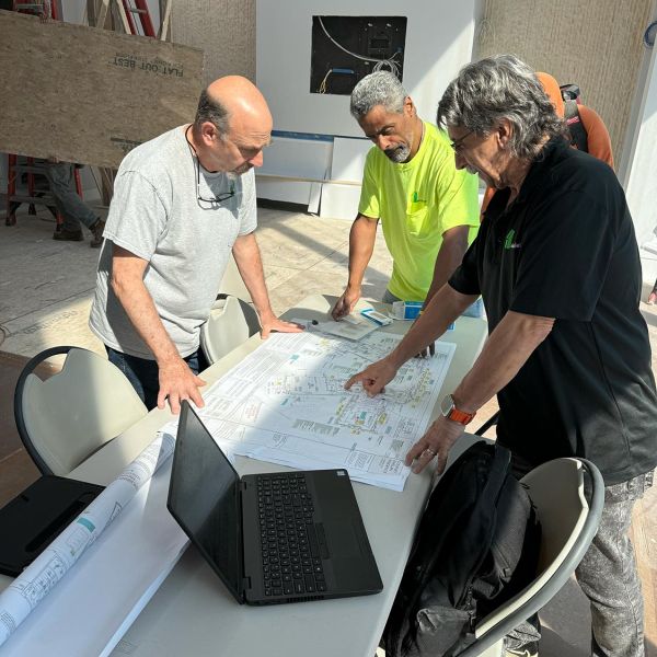 Three men examining a set of construction blueprints on a table in a building under construction.